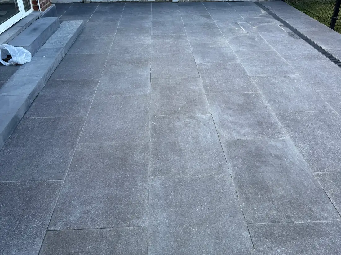 Opritreiniging — Het natuurstenen terras: de groene afdruk van een tuintafel die er jaren heeft gestaan. — na