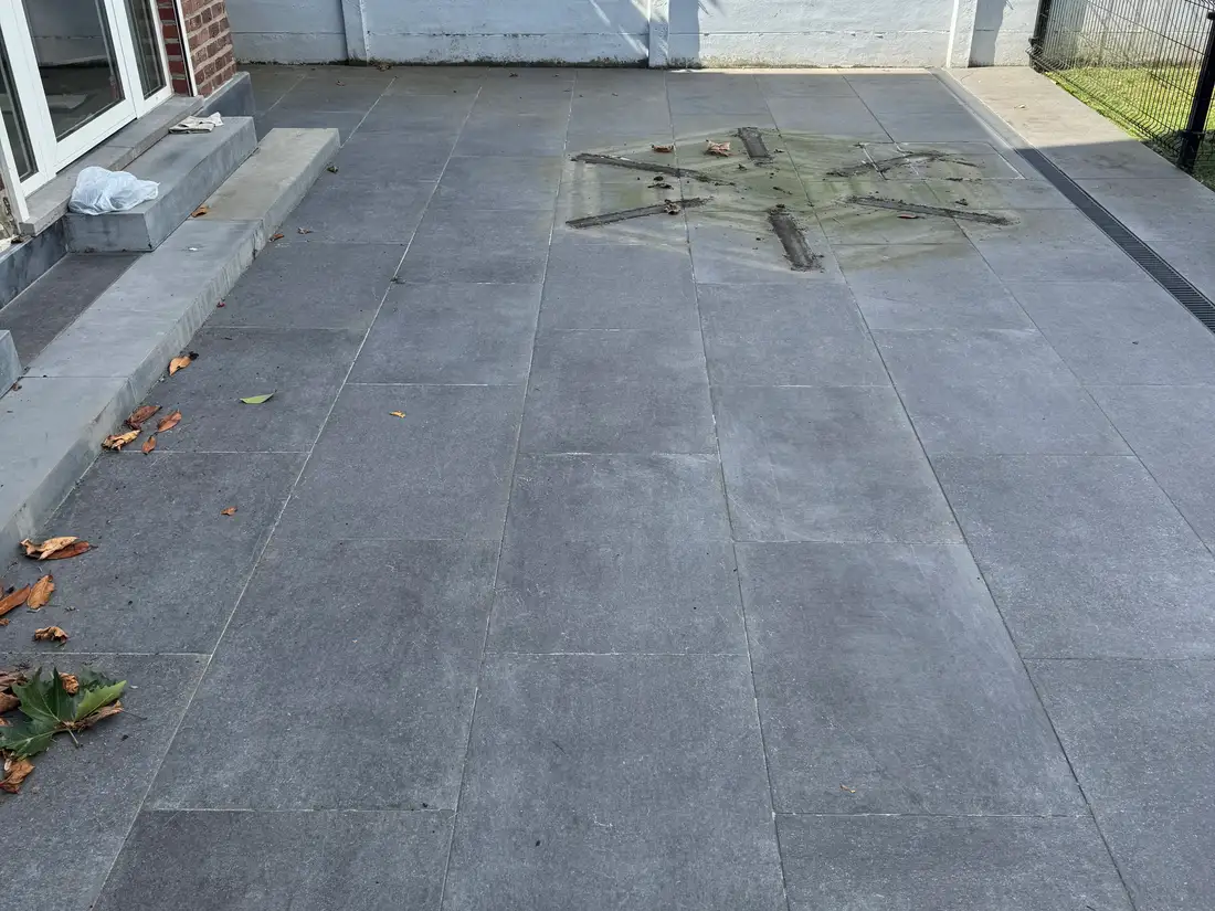 Opritreiniging — Het natuurstenen terras: de groene afdruk van een tuintafel die er jaren heeft gestaan. — voor
